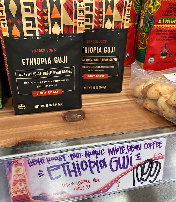 Two bags of Trader Joe's Ethiopia Guji 100% Arabica whole bean coffee displayed on a wooden shelf with a price tag showing $10.99.