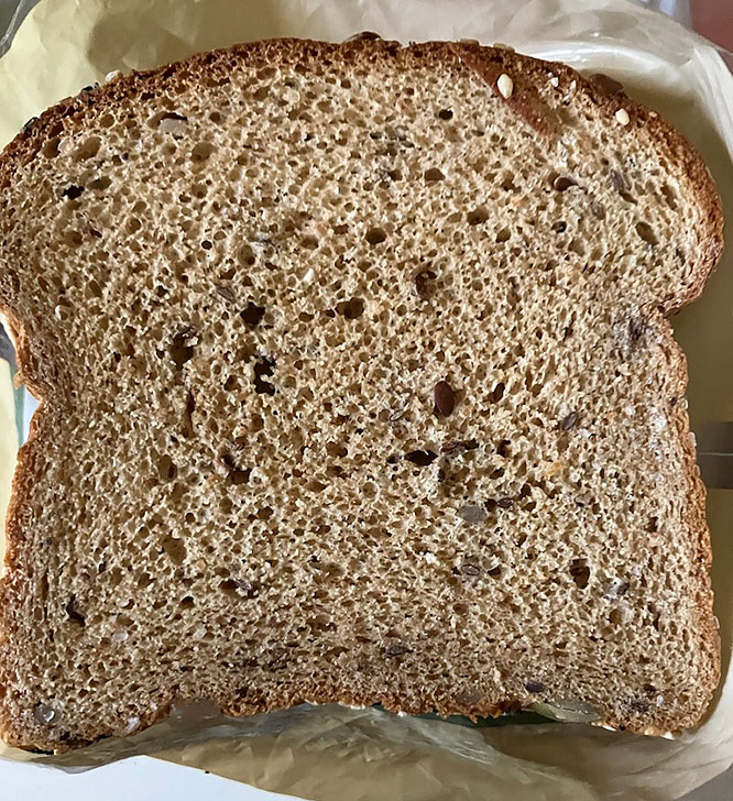 Top view of a slice of brown bread with seeds and a textured surface.