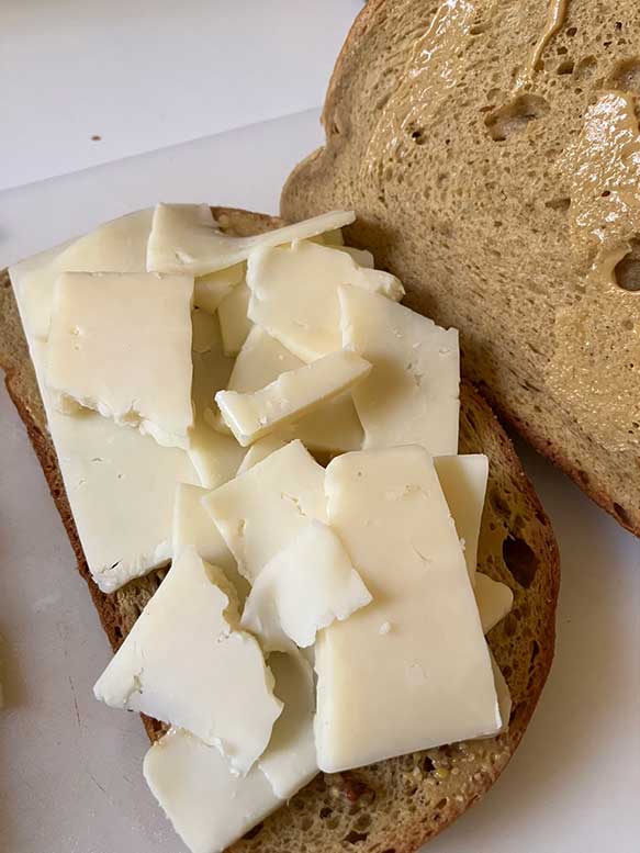 A slice of whole grain bread with large pieces of white cheese on top, partially covered by another slice of bread.